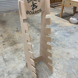 May include: A wooden skateboard rack with a sign that says "Skate Boards" and a graphic of a person skateboarding. The rack has 10 slots for skateboards.