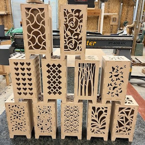 May include: Ten wooden lampshades with different laser cut designs. The lampshades are all the same size and shape, and they are arranged in two rows of five. The designs include hearts, geometric patterns, trees, butterflies, and flowers.