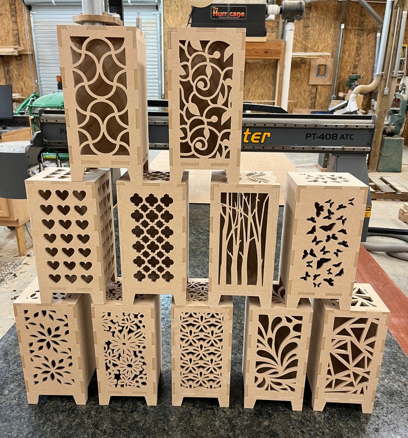 May include: Ten wooden lampshades with different laser cut designs. The lampshades are all the same size and shape, and they are arranged in two rows of five. The designs include hearts, geometric patterns, trees, butterflies, and flowers.