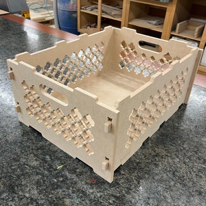 May include: A wooden crate with a decorative lattice pattern. The crate is made of light brown wood and has a rectangular shape. The crate has a handle on the top.