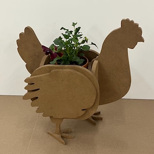 Puede incluir: Un macetero de madera con forma de pollo con un acabado marrón. El macetero tiene un hueco para una maceta y se muestra una pequeña planta en el macetero. El macetero con forma de pollo es una excelente manera de agregar un toque de fantasía a la decoración de tu hogar.