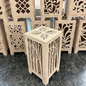 May include: A set of wooden candle holders with intricate laser cut designs. The designs include floral patterns, geometric shapes, and a tree branch pattern.