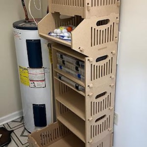 May include: A tall, unfinished wooden storage unit with multiple shelves and compartments. The unit has a slotted design and is filled with various items, including fishing tackle boxes and golf balls. It stands next to a water heater.
