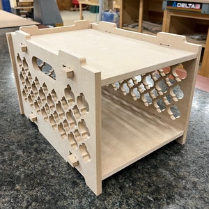 May include: A two-tiered wooden shelf unit with a decorative cutout pattern. The shelf is made of unfinished wood and has a simple, modern design.