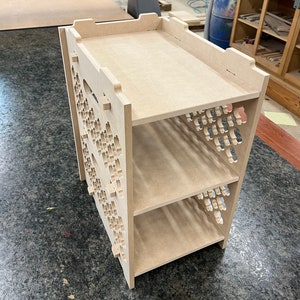 May include: A wooden shelf unit with three shelves and a decorative cutout pattern on the sides. The shelves are made of unfinished wood and are ready to be stained or painted.