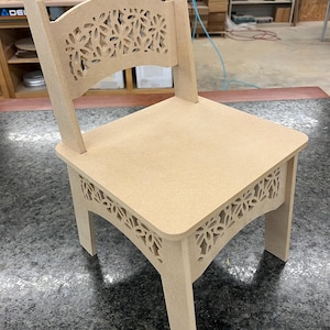 May include: A light brown wooden chair with a decorative cutout design on the back and sides. The chair has a square seat and four legs.