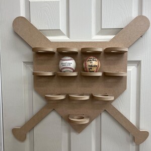 May include: A baseball-themed display shelf in the shape of a baseball bat and home plate. The shelf is made of light brown wood and features multiple circular shelves to hold baseballs. Two baseballs are displayed, one with the text "Official League Genuine Leather".