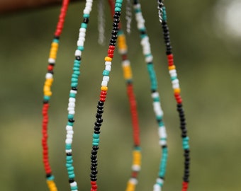May include: Three beaded necklaces with black, white, red, yellow, and turquoise beads. The necklaces are hanging from a rusty metal bar.