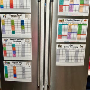 May include: A stainless steel refrigerator with six magnetic inventory sheets attached to the front. The sheets are titled Freezer Beef, Lamb, Chicken, Hog, Frozen Favorites, Garden Goodness, and Wild Game, featuring colorful grids for tracking food items.