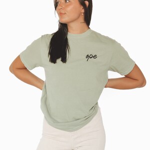 Peut inclure: Un t-shirt vert sauge avec le mot "ope" brodé sur la poitrine gauche.