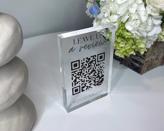 May include: A clear acrylic sign with black text that reads "LEAVE US a review" and a black and white QR code. The text "SCENTED SERENADE" is printed below the QR code.