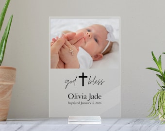 May include: A white acrylic plaque with a photo of a baby girl, the text "god bless", a cross, the name "Olivia Jade", and the date "baptized January 4, 2024".