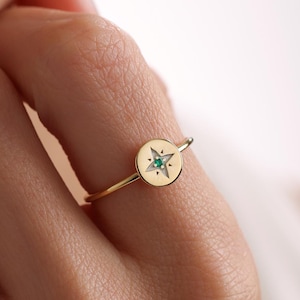 May include: A gold ring with a round, flat top featuring a five-pointed star with a green gemstone in the center.