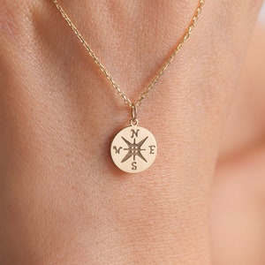 May include: A gold necklace with a compass pendant. The compass has the letters N, S, E, and W engraved on it.