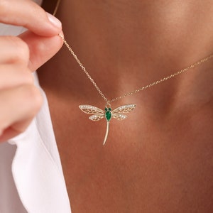 May include: A gold necklace with a dragonfly pendant featuring green and white gemstones.
