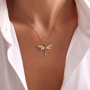 May include: A gold necklace with a dragonfly pendant featuring a red gemstone. The dragonfly has intricate details and a delicate design.