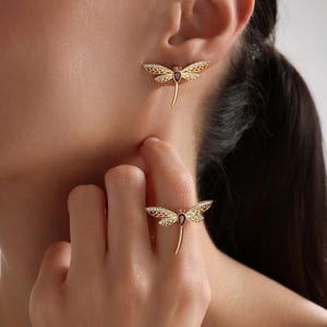 May include: A gold dragonfly ring and earrings set with a red gemstone. The dragonfly wings are detailed with white stones. Save 9% with a Triple Set Necklace - Ring - Earrings.