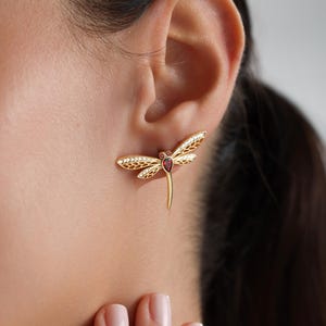 May include: Gold dragonfly earrings with a red gemstone in the center and clear rhinestones on the wings.