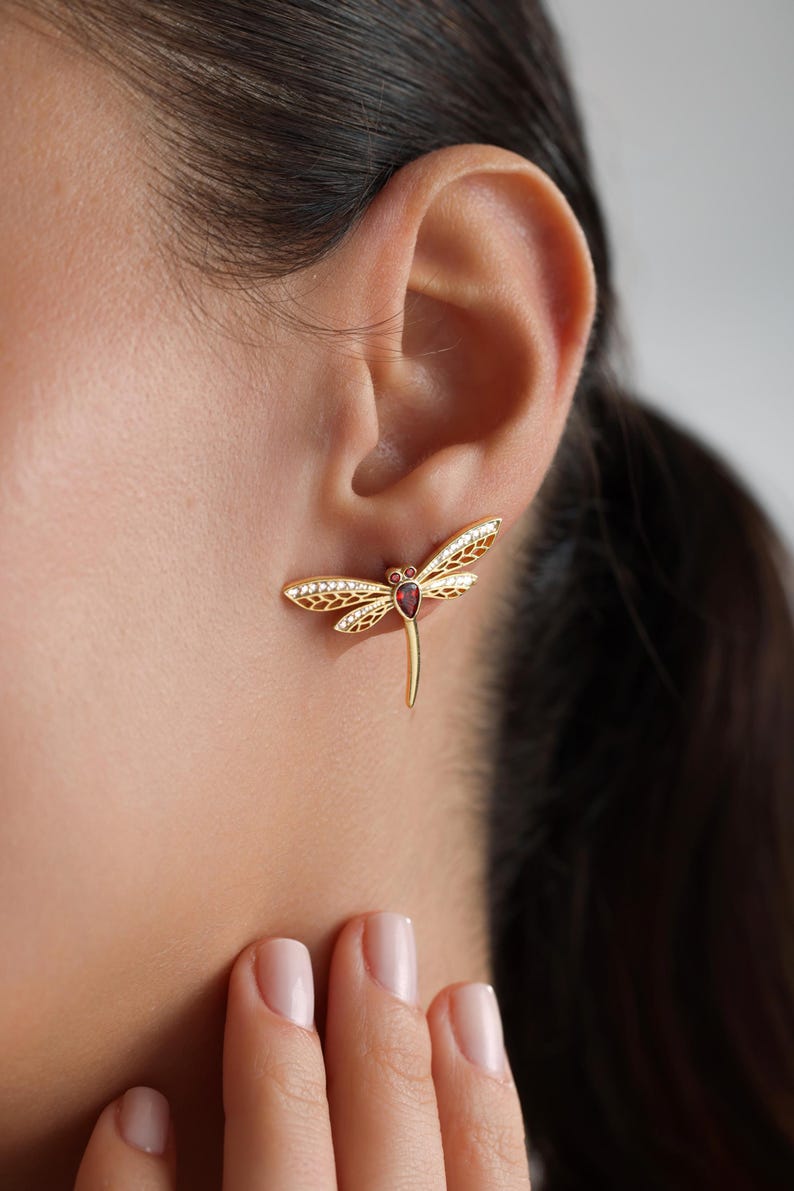 May include: Gold dragonfly earrings with a red gemstone in the center and clear rhinestones on the wings.