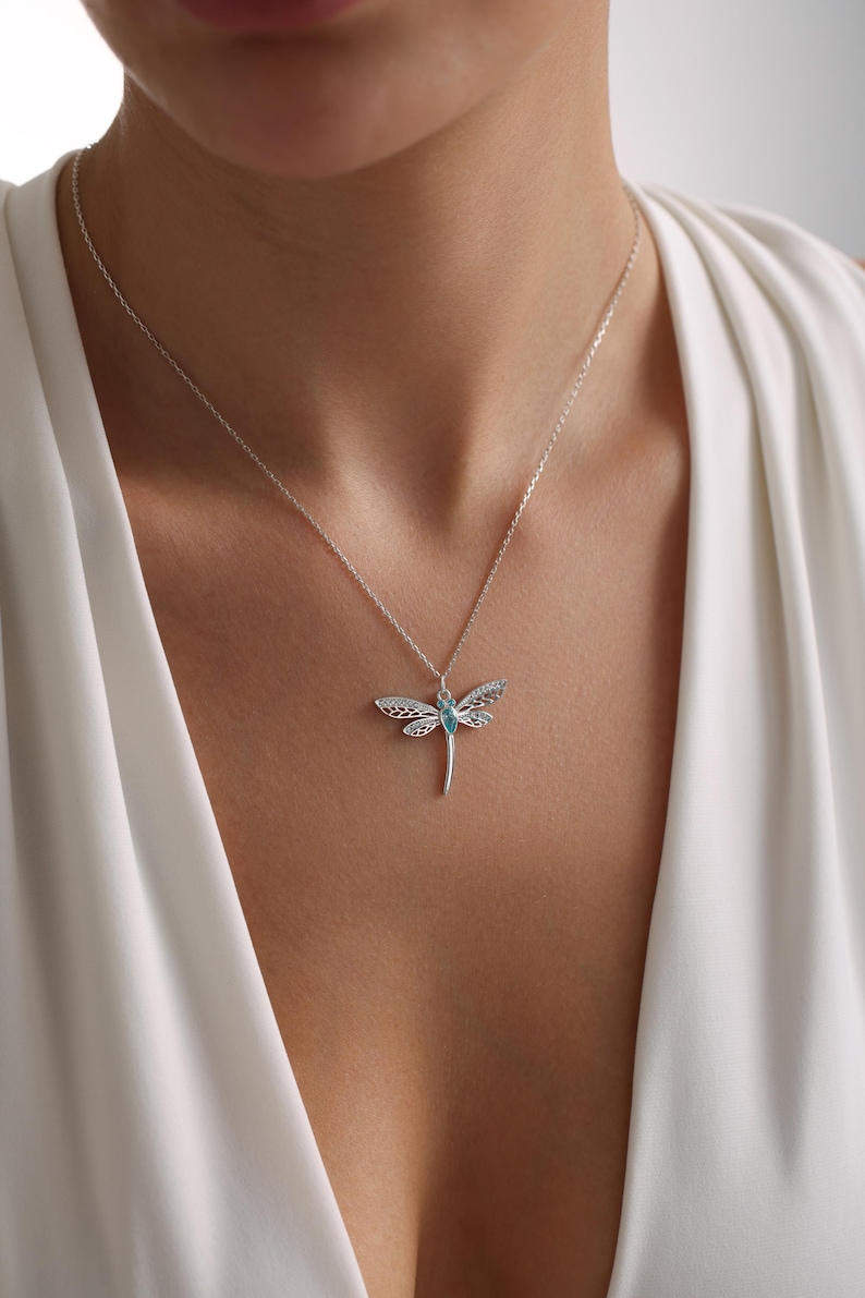 May include: A silver necklace with a dragonfly pendant featuring a blue gemstone. The dragonfly has intricate details and a delicate design.
