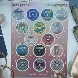 May include: A pink and white illustrated poster with a discography of Stray Kids albums. The poster features 12 circular images of album covers with the album titles written on them. The album titles include "Mixtape", "I am NOT", "I am WHO", "I am YOU", "Clé 1: MIROH", "Clé 2: YELLOW WOOD", "Levanter", "GO生", "SKZ2020", "NOEASY", "ODINARY", "MAXIDENT", "CIRCUS", and "★★★★★". The poster also includes the text "straykids" and "discography" at the top and "@fromthestarsco" at the bottom.