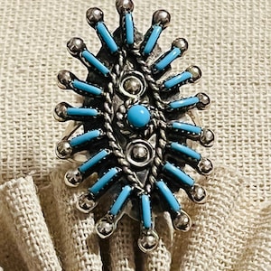 May include: A silver ring with a turquoise stone in the center and a design of turquoise and silver rays radiating out from the center.