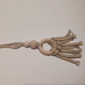 May include: A beige macrame wall hanging with a wooden ring and beads. The design features a knotted rope pattern with a fringe of loose cords. The natural tones and textures create a bohemian aesthetic.