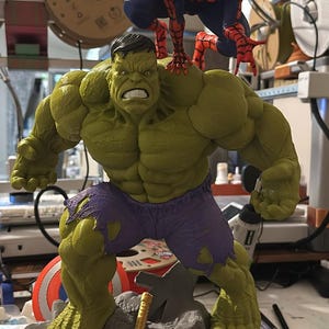 Può includere: Una statuina dettagliata con Hulk, con Spider-Man appollaiato sulla sua spalla. Hulk è verde con pantaloni viola, in piedi su una base rocciosa. È presente anche il martello di Thor. Un oggetto da collezione creativo.