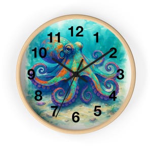 Op de afbeelding: Een ronde wandklok met een licht houten frame. De wijzerplaat toont een kleurrijke octopus-illustratie in blauwe, oranje en paarse tinten tegen een turquoise achtergrond. Zwarte wijzers geven de tijd aan.