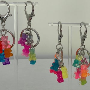 May include: Two silver keychains with colorful gummy bear charms. The keychains have a silver ring and a silver lobster clasp. The gummy bears are in various colors, including red, orange, yellow, green, blue, purple, and pink.