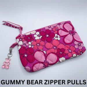May include: Pink quilted zipper pouch with a floral print and a pink gummy bear zipper pull.