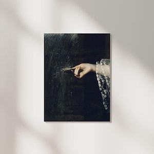 May include: A close-up of a hand reaching out from a dark background, wearing a white lace sleeve. The hand is pointing with its index finger, and the background is blurred.