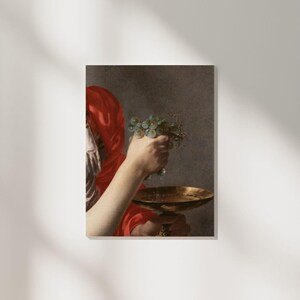 Puede incluir: Una mujer con una túnica roja sostiene un racimo de uvas verdes sobre un cuenco dorado. Las uvas gotean en el cuenco.