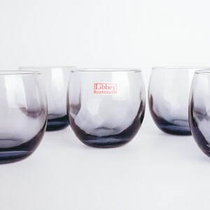 Pu&ograve; includere: Sei bicchieri trasparenti in vetro con una leggera sfumatura grigia fum&egrave;. I bicchieri sono disposti in fila su una superficie bianca. Il bicchiere centrale ha un'etichetta rossa con la scritta "Libbey Glassware".