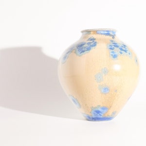 May include: A cream-coloured ceramic vase with a blue and white glaze pattern. The vase has a rounded body and a wide opening.