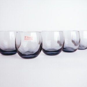 Pu&ograve; includere: Sei bicchieri di vetro trasparente con una forma leggermente arrotondata. I bicchieri sono disposti in fila e hanno una tinta blu scuro. Il bicchiere al centro ha un'etichetta rossa che recita "Libbey Glassware".