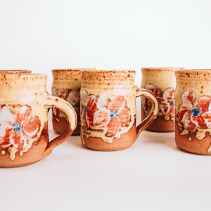 May include: Set of five ceramic mugs with a yellow glaze and floral designs in shades of red, orange, blue, and white.