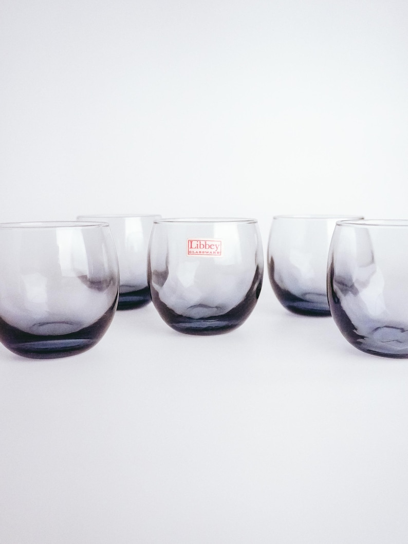 Pu&ograve; includere: Sei bicchieri trasparenti in vetro con una leggera sfumatura grigia fum&egrave;. I bicchieri sono disposti in fila su una superficie bianca. Il bicchiere centrale ha un'etichetta rossa con la scritta "Libbey Glassware".