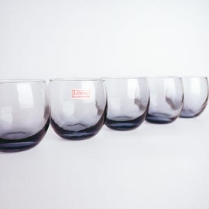 Pu&ograve; includere: Cinque bicchieri di vetro trasparente con una tinta blu. Il bicchiere al centro ha un'etichetta rossa "Libbey Glassware".