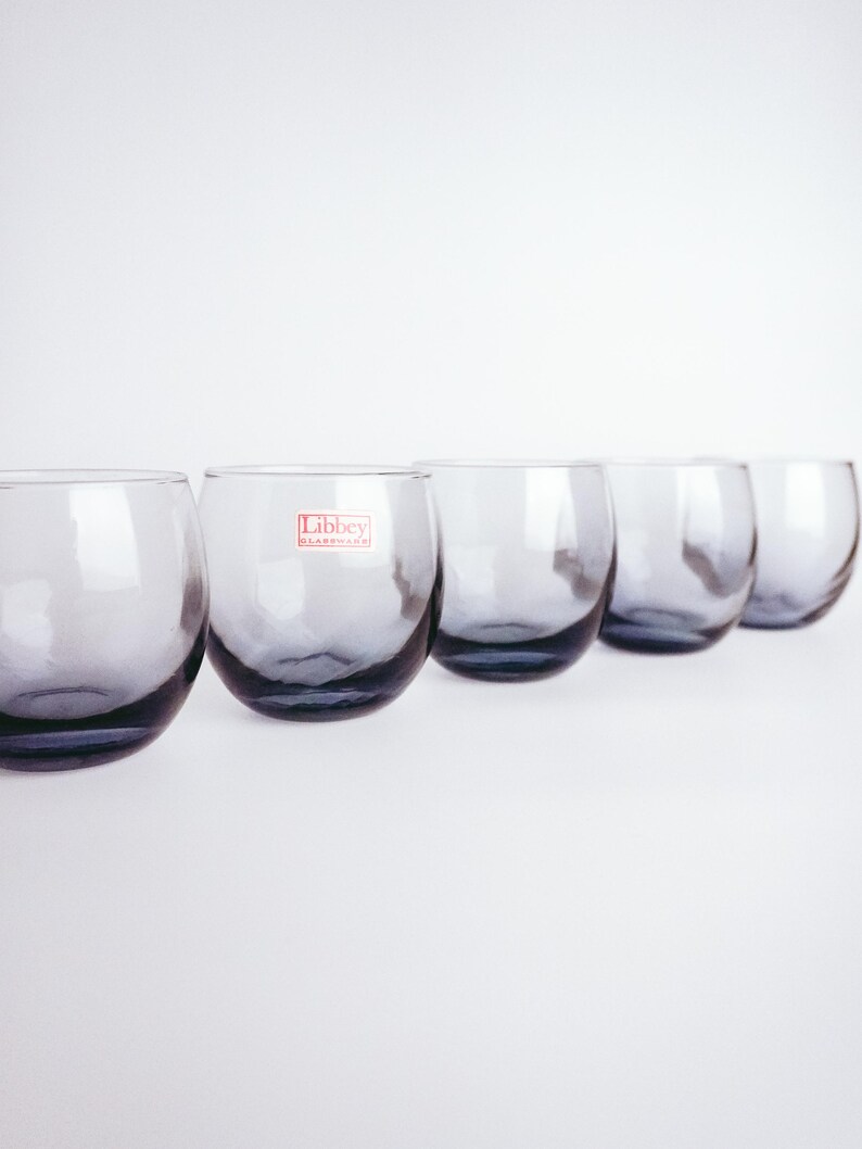 Pu&ograve; includere: Cinque bicchieri di vetro trasparente con una tinta blu. Il bicchiere al centro ha un'etichetta rossa "Libbey Glassware".