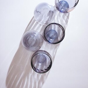 Pu&ograve; includere: Quattro bicchieri di vetro trasparente con una tinta viola. I bicchieri sono disposti in una linea verticale, con il bicchiere superiore leggermente spostato a destra. I bicchieri sono su uno sfondo bianco.