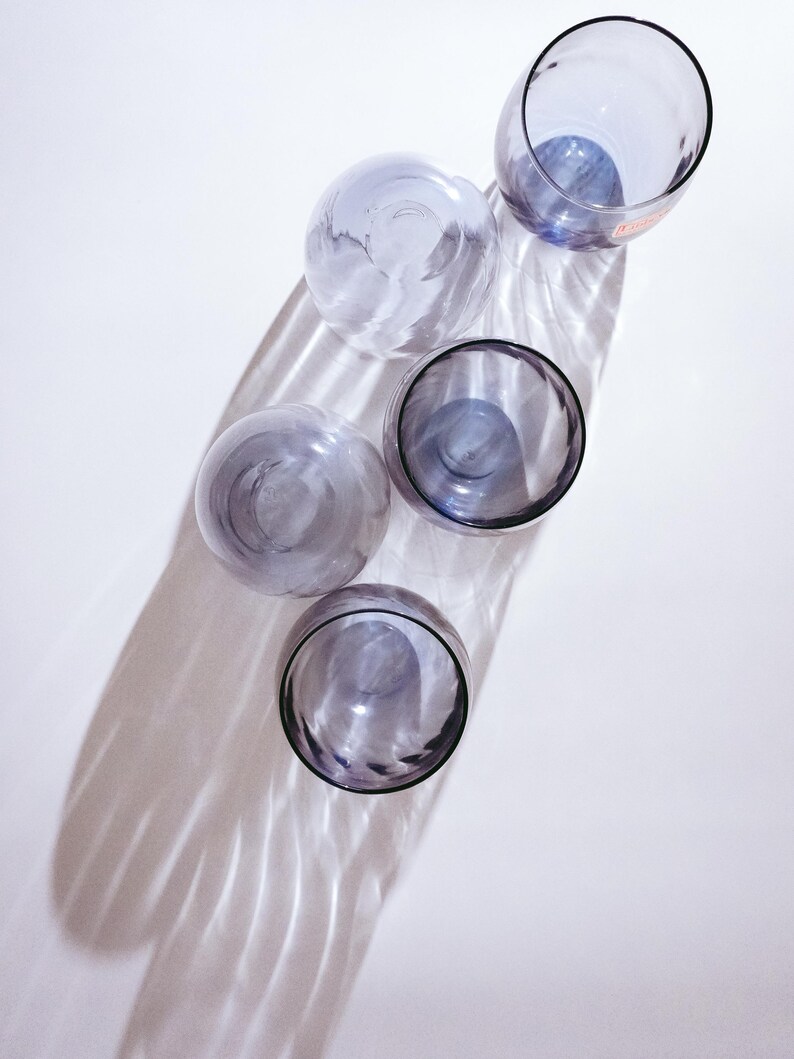 Pu&ograve; includere: Quattro bicchieri di vetro trasparente con una tinta viola. I bicchieri sono disposti in una linea verticale, con il bicchiere superiore leggermente spostato a destra. I bicchieri sono su uno sfondo bianco.