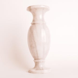 May include: A white marble vase with a classic design. The vase has a wide base and a narrow neck, and it is decorated with subtle veining.