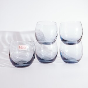 Pu&ograve; includere: Set di sei bicchieri di vetro trasparente con una tinta blu. I bicchieri sono impilati in due gruppi di tre. I bicchieri hanno una forma arrotondata e un piccolo bordo. I bicchieri sono realizzati da Libbey Glass.