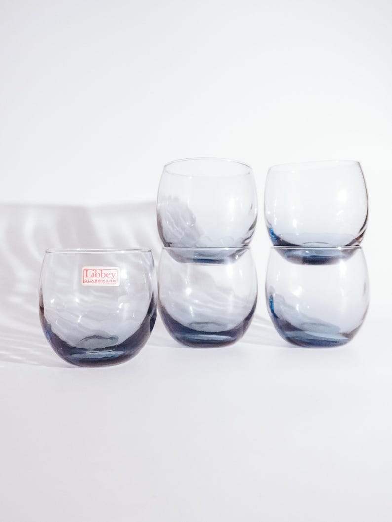 Pu&ograve; includere: Set di sei bicchieri di vetro trasparente con una tinta blu. I bicchieri sono impilati in due gruppi di tre. I bicchieri hanno una forma arrotondata e un piccolo bordo. I bicchieri sono realizzati da Libbey Glass.