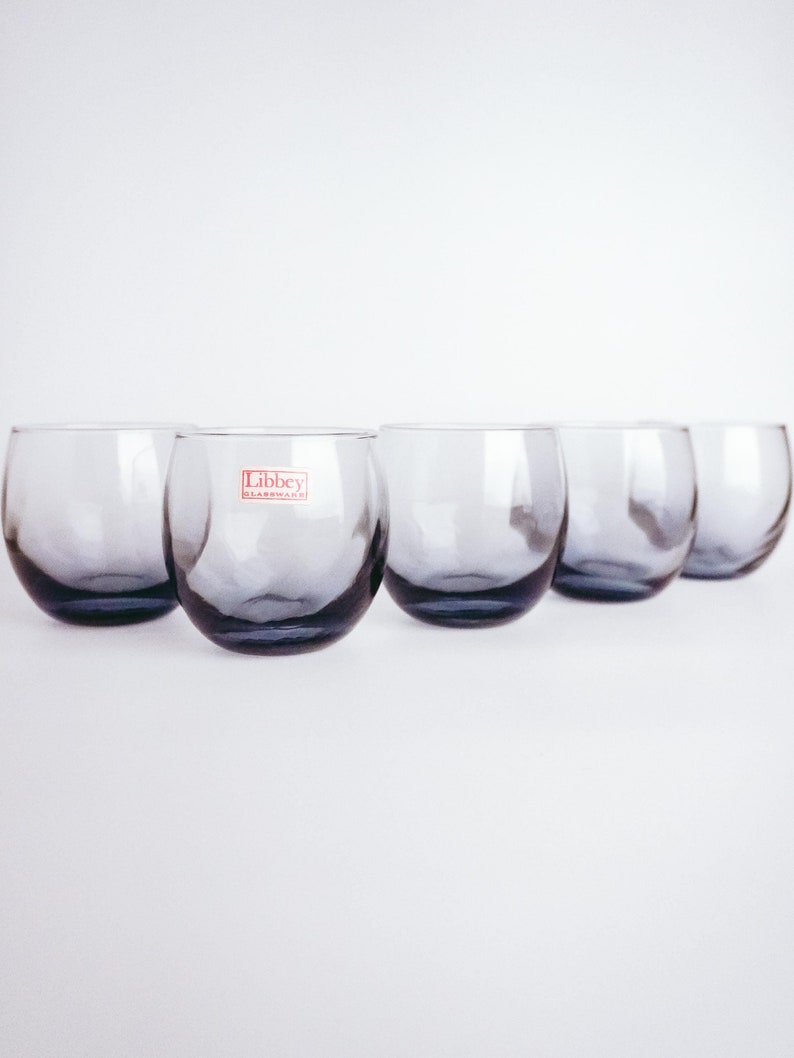 Pu&ograve; includere: Sei bicchieri di vetro trasparente con una forma leggermente arrotondata. I bicchieri sono disposti in fila e hanno una tinta blu scuro. Il bicchiere al centro ha un'etichetta rossa che recita "Libbey Glassware".