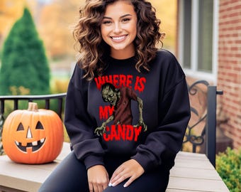 Puede incluir: Sudadera negra con el texto rojo "WHERE IS MY CANDY" y un gráfico de zombi. Una calabaza naranja tallada con una cara está cerca. Parte de una colección con temática de Halloween.