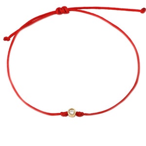 May include: A red string bracelet with a small gold bead set with a clear gemstone.
