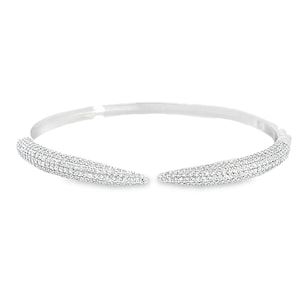 May include: A silver-toned open cuff bracelet featuring two tapered, curved ends. The entire surface of the two curved ends is densely encrusted with small, clear, sparkling stones that create a reflective, textured appearance against the metal.
