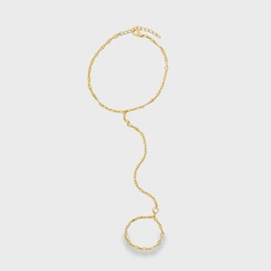 May include: A gold-toned hand chain featuring a delicate circular wrist bracelet connected by a slender, wavy chain link to a smaller circular ring component. The jewelry piece is constructed from thin, polished metal links with a consistent finish.